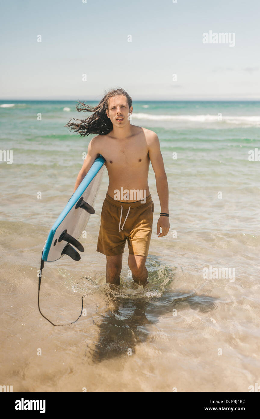 Giovane uomo con la tavola da surf in piedi in oceano su giorno di estate Foto Stock