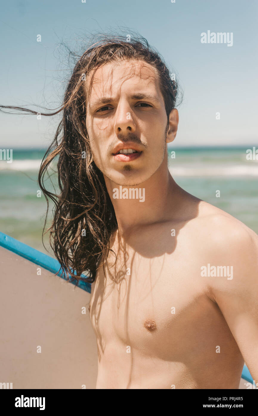 Ritratto di giovane uomo con la tavola da surf con l'oceano sullo sfondo sul giorno di estate Foto Stock
