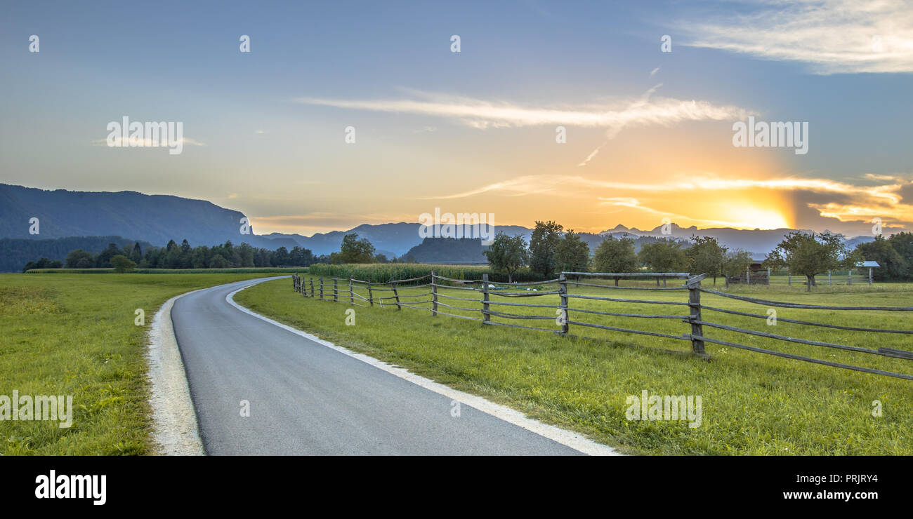 Strada secondaria attraverso la campagna slovena il paesaggio con le Alpi Giulie sullo sfondo vicino a Bled Foto Stock
