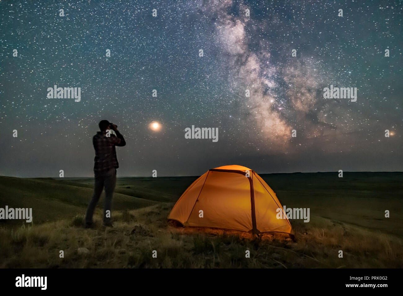 Un interprete di stazionamento comporta per una scena in praterie National Park, Saskatchewan, di guardare le stelle con un binocolo sotto la Via Lattea su una notte senza luna n Foto Stock