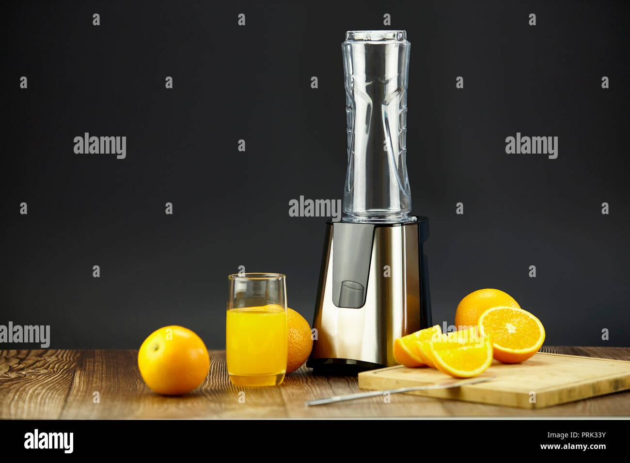 Frullatore e succo d'arancia con arance fresche sulla tavola con sfondo nero. Foto Stock