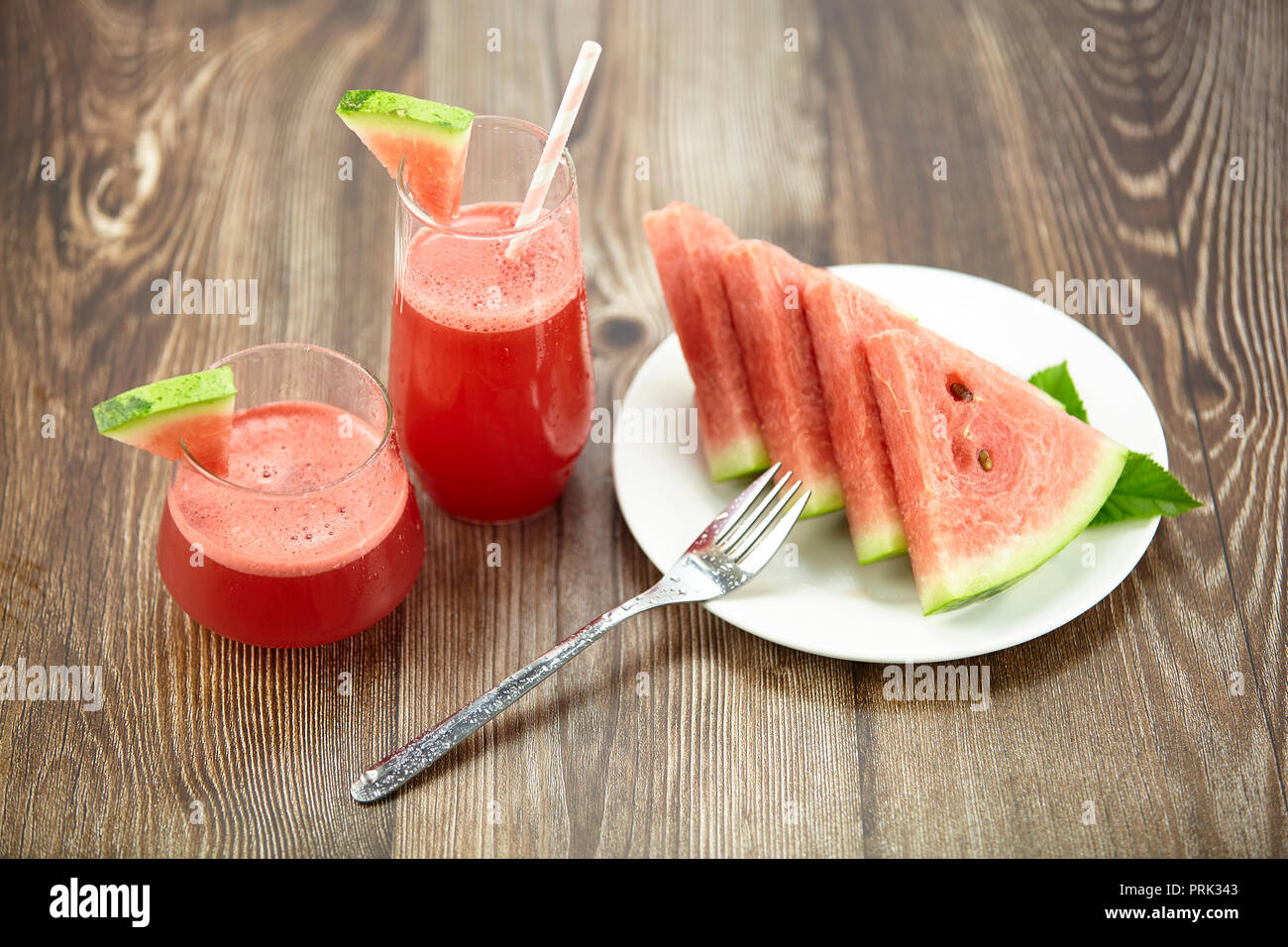 Due bicchieri di acqua succo di melone con acqua fette di melone su una piastra sul disco superficie di legno. Foto Stock