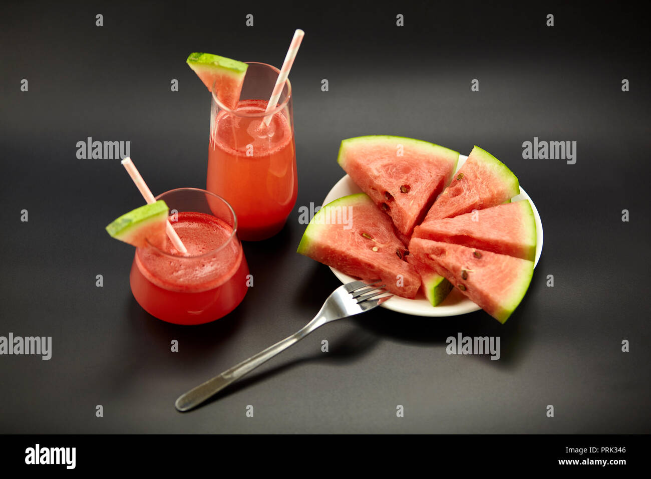 Due bicchieri di acqua succo di melone con acqua fette di melone su una piastra su sfondo nero. Foto Stock