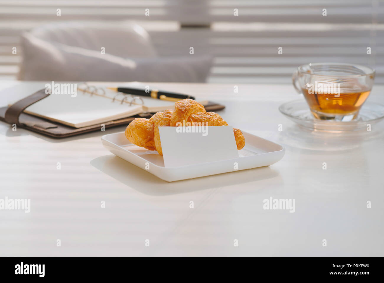 La mattina la colazione nel salotto con croissant francesi, tazzina, penna e note libro sul tavolo di pietra Foto Stock