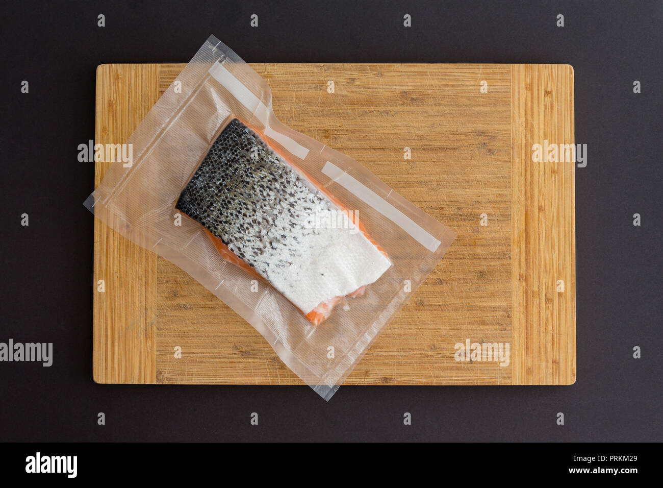 La porzione di gourmet freschi Salmone atlantico in un pacchetto vuoto di plastica chiara pronto fro congelamento giacente su un bordo di bambù su uno sfondo nero Foto Stock