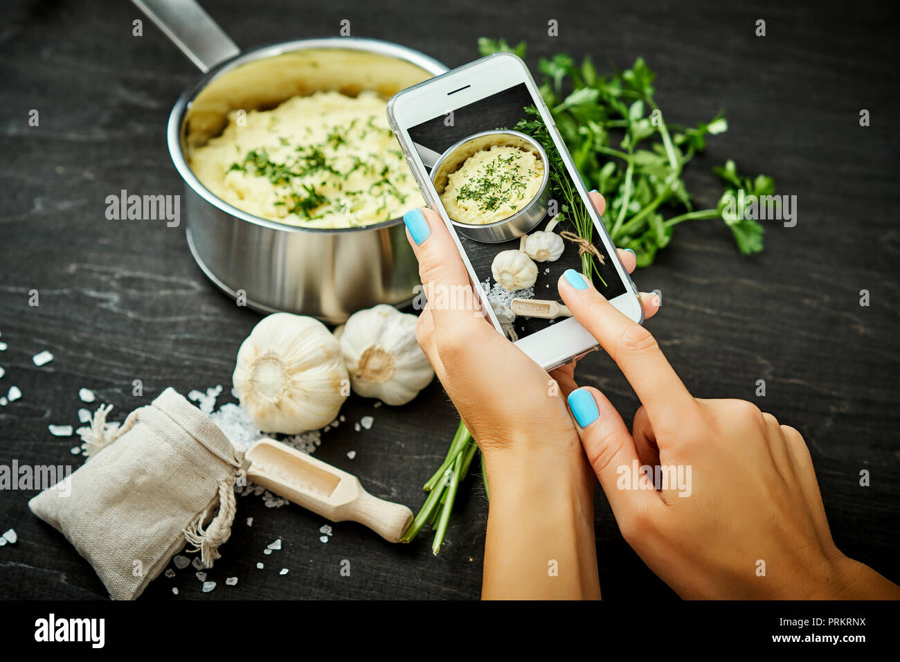 La donna ha le mani tenendo il telefono cellulare e scattare una foto di una deliziosa purea di patate su una tavola di legno Foto Stock