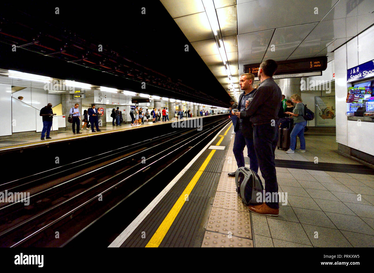 Persone in attesa sulla piattaforma di una stazione della metropolitana di Londra, Londra, Inghilterra, Regno Unito. Foto Stock