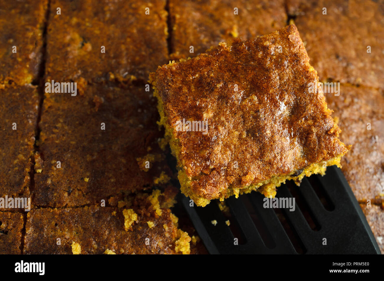 Una fetta di cotto domestico torta di carote che viene sollevato da un blocco che è stato tagliato in quadrati, con sparse briciole. Fotografato dal di sopra. Foto Stock