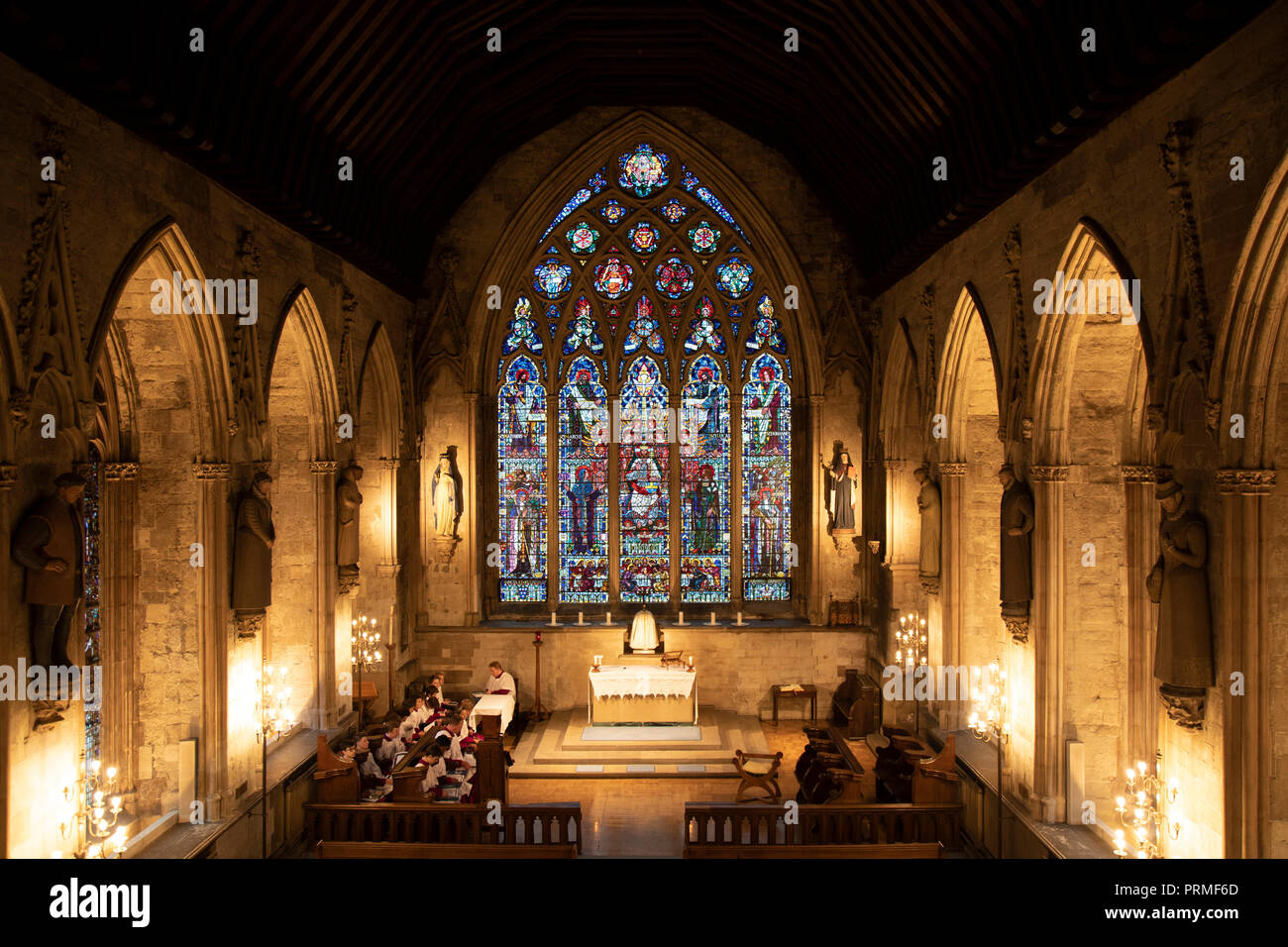 Coro pratica accanto alla finestra di vetro colorato nella cappella principale presso il St Etheldreda la Chiesa a Londra, Inghilterra, Regno Unito. St Etheldreda la chiesa fu la cappella della città dei vescovi di Ely da circa 1250 a 1570. Essa è la più antica chiesa cattolica in Inghilterra e solo uno dei due restanti edifici a Londra dal regno di Edward I. che una volta era uno dei più influenti luoghi di Londra con un palazzo di un vasto terreno. Era come uno stato indipendente, il Vescovo di Ely's Place a Londra o a Ely Place come viene ora chiamato, e la sua cappella ha preso il suo nome da uno di Inghilterra più popolare sain Foto Stock