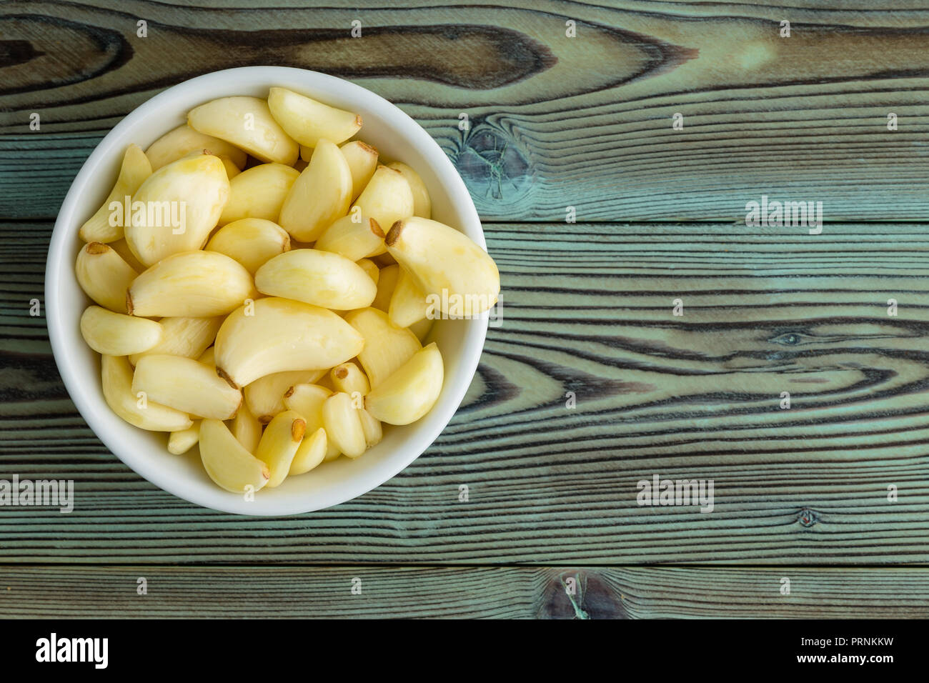 Appena sbucciata aromatico spicchi di aglio in un generico in ceramica bianca ramekin al lato di legno rustico visto dal di sopra Foto Stock