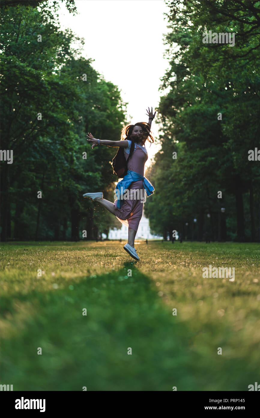 Basso angolo di visione della donna felice jumping con ampia bracci sul prato in posizione di parcheggio Foto Stock