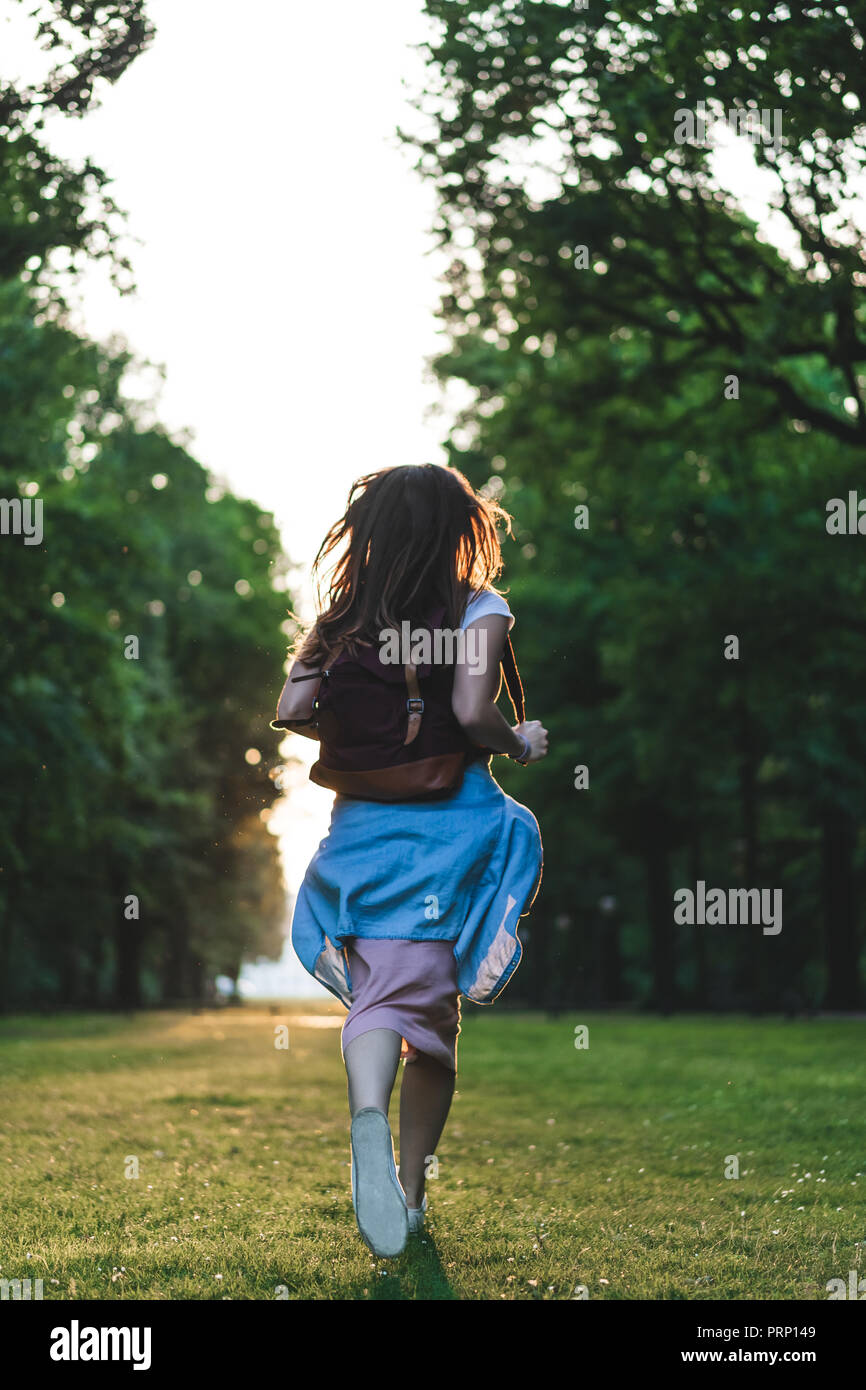 Vista posteriore della donna con zaino in esecuzione sul prato con alberi Foto Stock