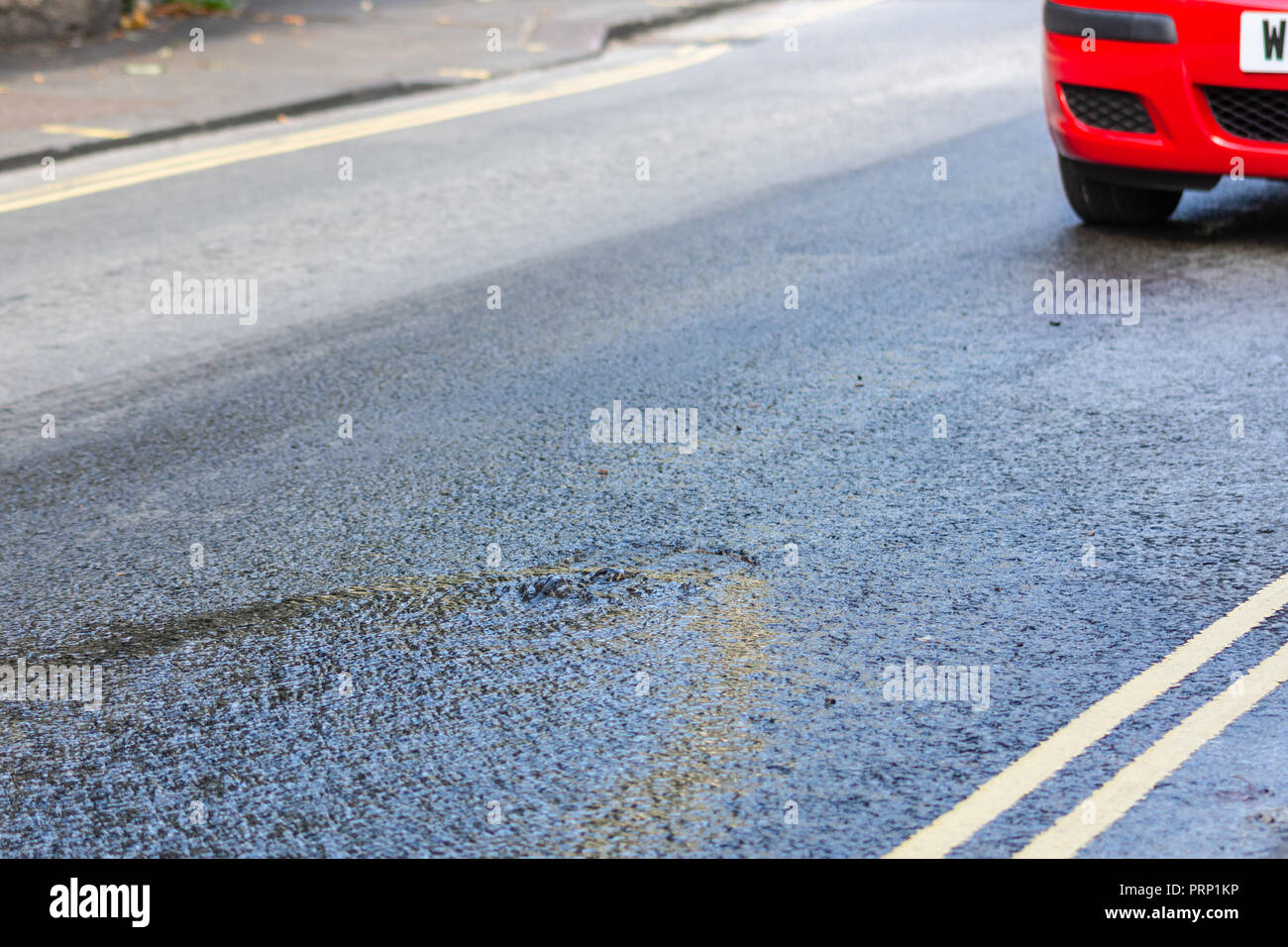 Acqua da una raffica di acqua provenienti principale attraverso un chiusino in mezzo alla strada e con vetture che passa su di essa Foto Stock