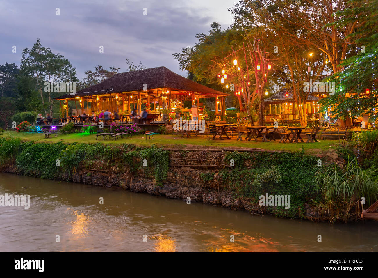 Serata di scena illuminata con un ristorante esterno dal fiume nella giungla tropicale, Pai, Thailandia Foto Stock