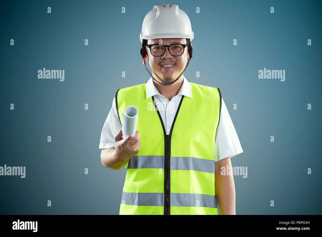 Ritratto di fiducioso asian giovane ingegnere di protezione da indossare elmetto e tenendo la carta cianografica . Foto Stock