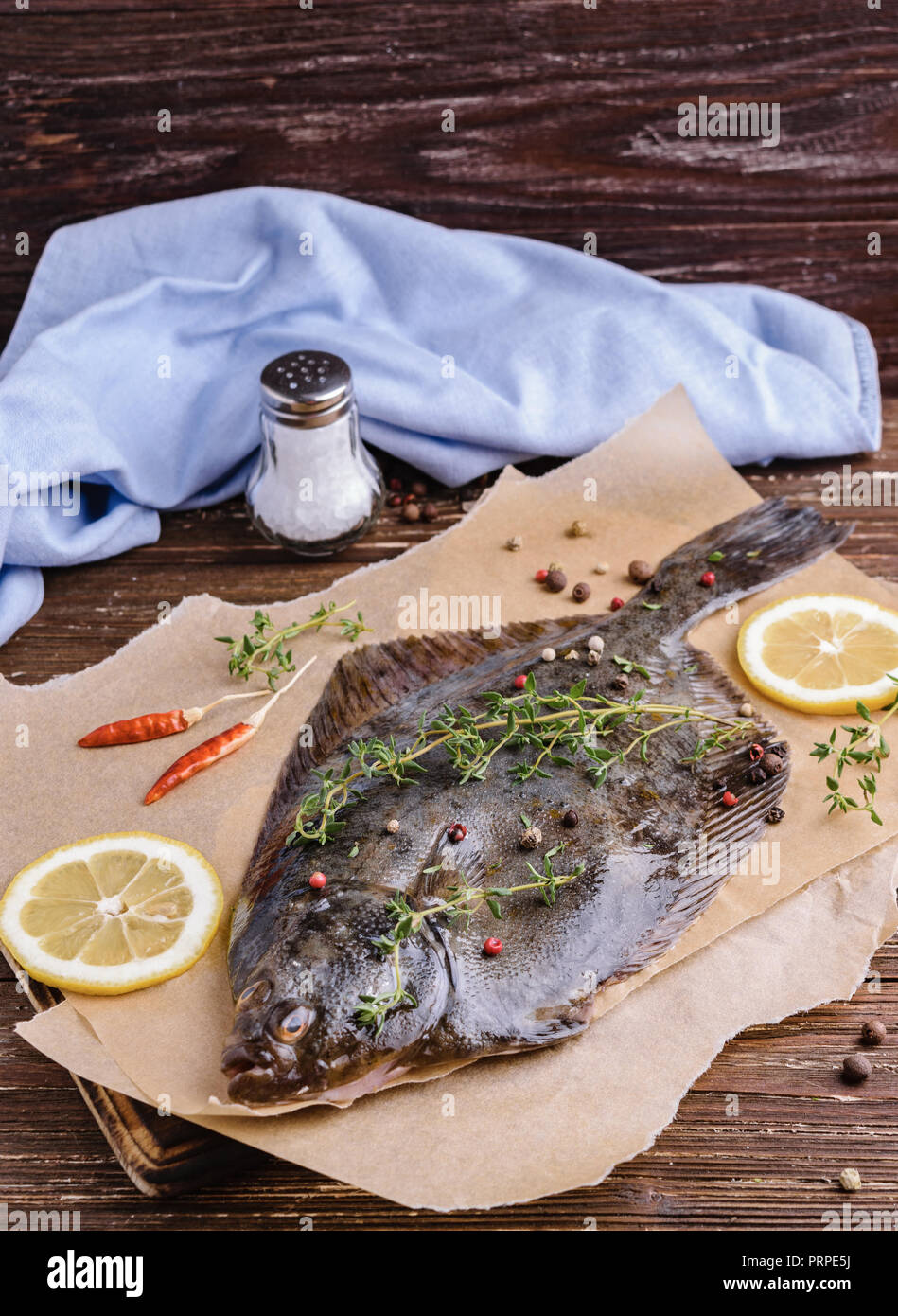 Materie passera di mare Passera di mare pesce (pesci piatti). Il processo di cottura del concetto. La Passera pianuzza Pesce con spezie, le fette di limone, timo su carta pergamena. Legno scuro tabella bac Foto Stock