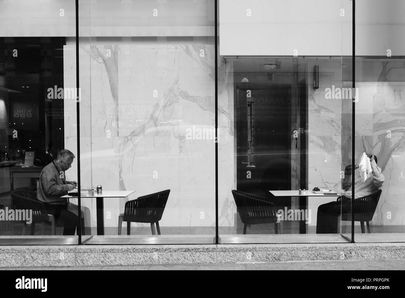 Candide di uomini anziani godere il loro pranzo separati in un centro per la cena. Uno è che copre la sua faccia con un tovagliolo come egli ha realizzato sto prendendo una foto. Foto Stock