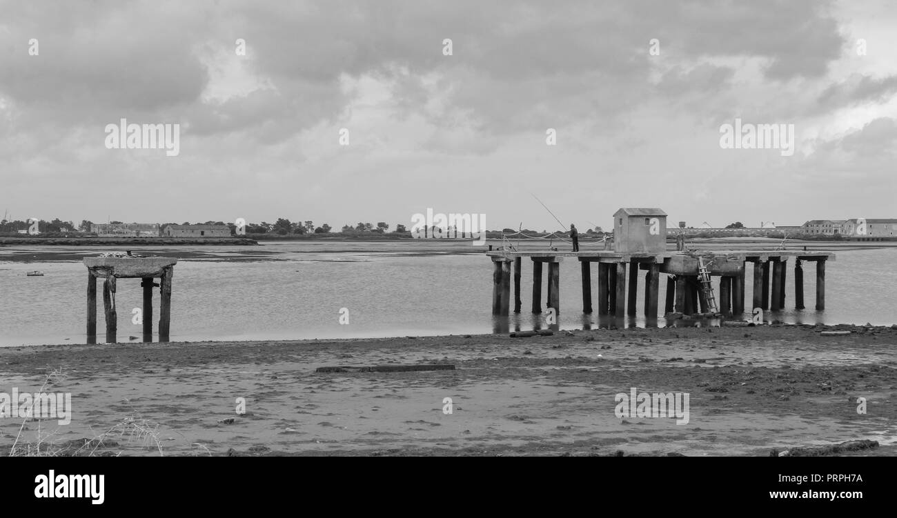 Abbandonato il dock sulla riva del fiume. Un pescatore vi è la pesca con un polo Foto Stock