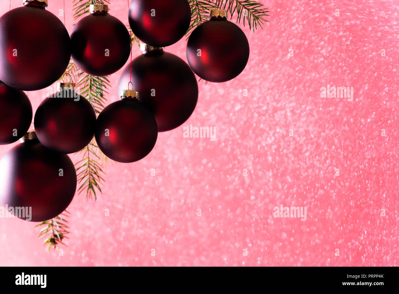 Elegante di colore rosso scuro palle di Natale appeso mentre nevicava, da una neve spray, in condizioni di luce intensa, perfetto per un Natale di biglietto di auguri o un banner. Foto Stock