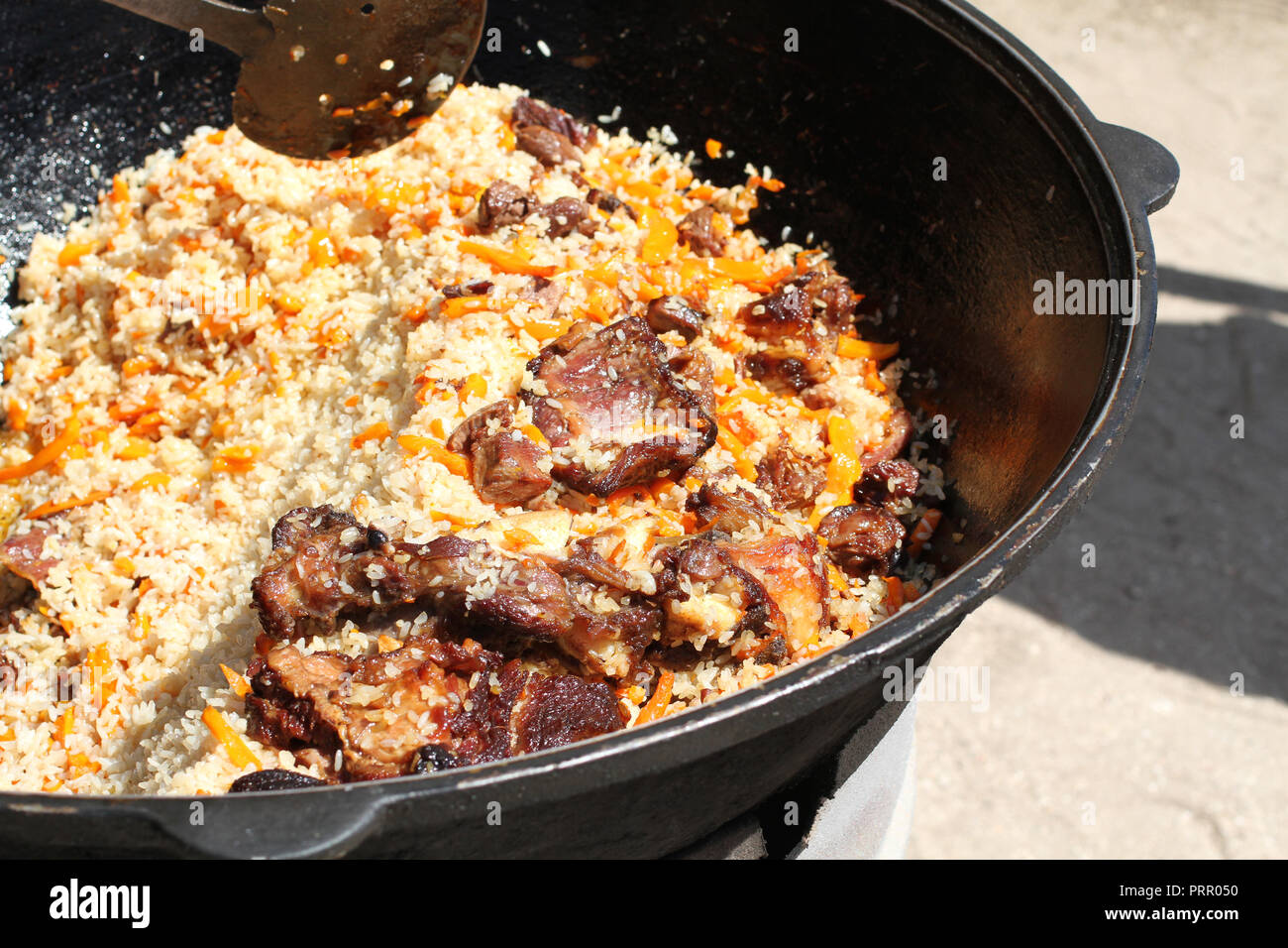 Tradizionale Uzbek pilaf con carne di agnello cucinata in un gran calderone Foto Stock