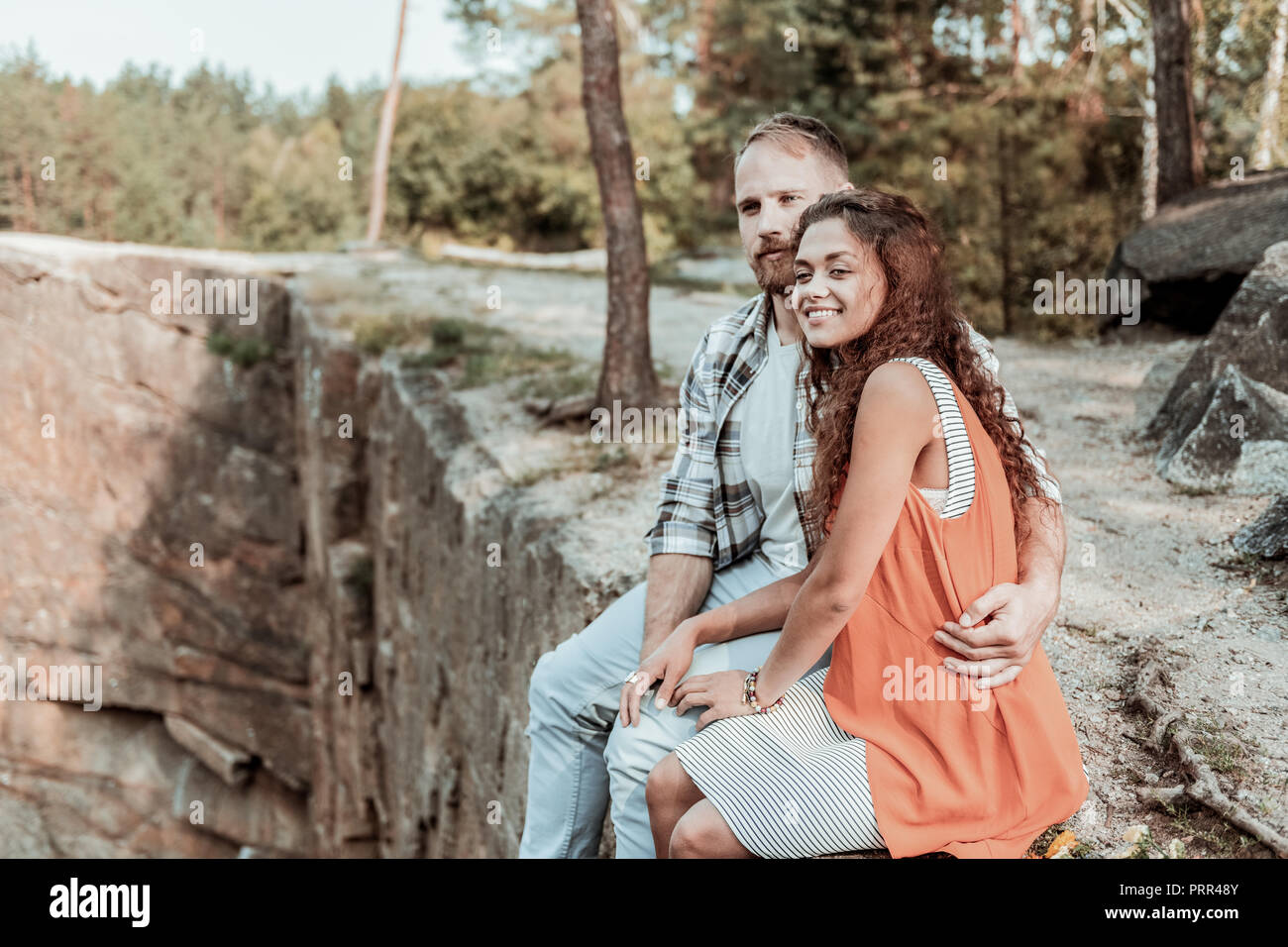 Barbuto bionda uomo abbraccia il suo sorridente ragazza mentre è seduto sulla roccia Foto Stock