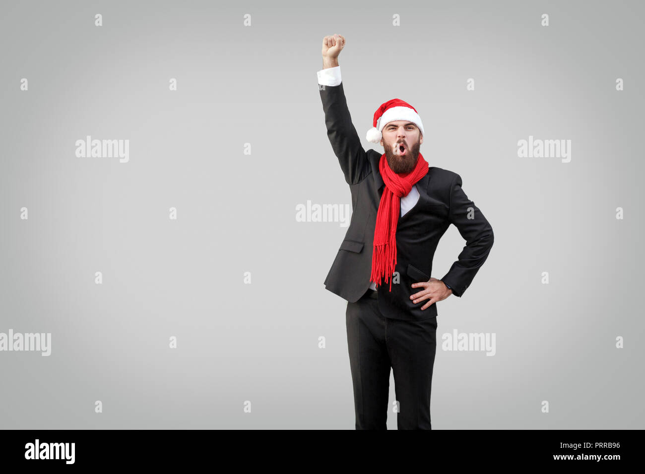 Hero stile. Imprenditore con la barba in classico abito nero, sciarpa rossa e nuovo anno hat rallegrandosi per il suo successo, gridando e guardando la fotocamera. Isolat Foto Stock