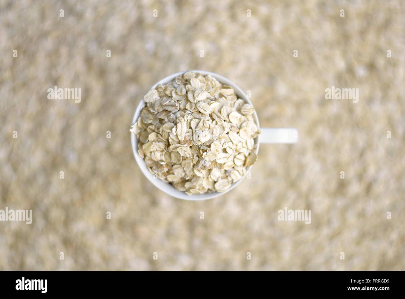 Tazza bianca piena di farina di avena su uno sfondo di farina di avena Foto Stock