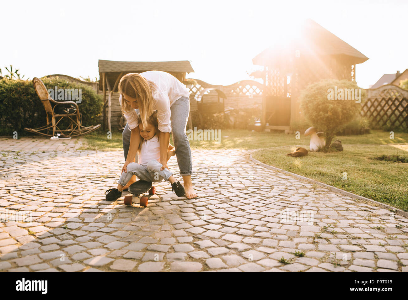 Madre aiutare piccola figlia di skateboard sul cortile sul giorno di estate Foto Stock