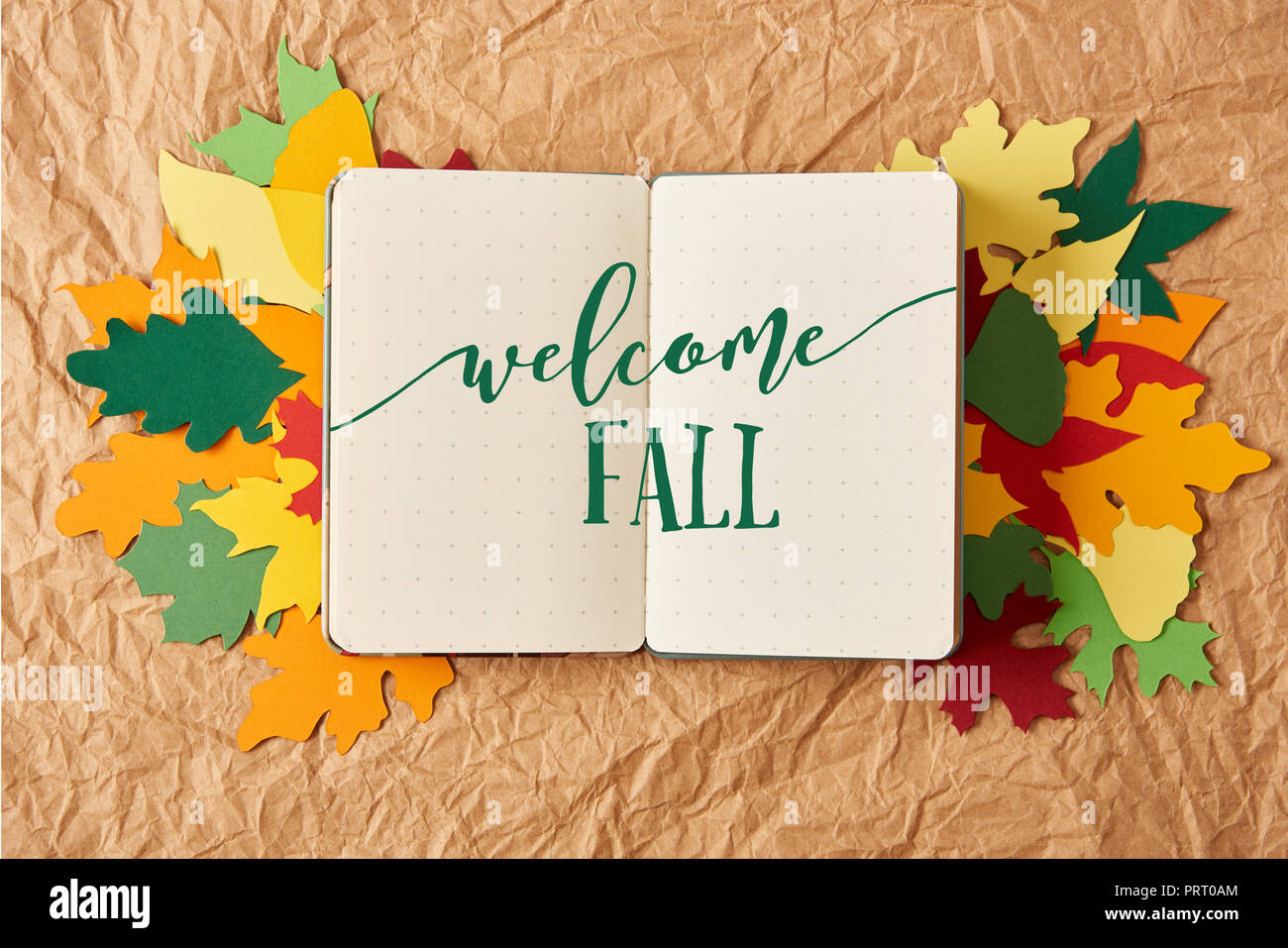 Vista superiore del notebook con " Benvenuto autunno" scritte sulla colorata a mano di foglie di carta su carta sgualcita sfondo Foto Stock
