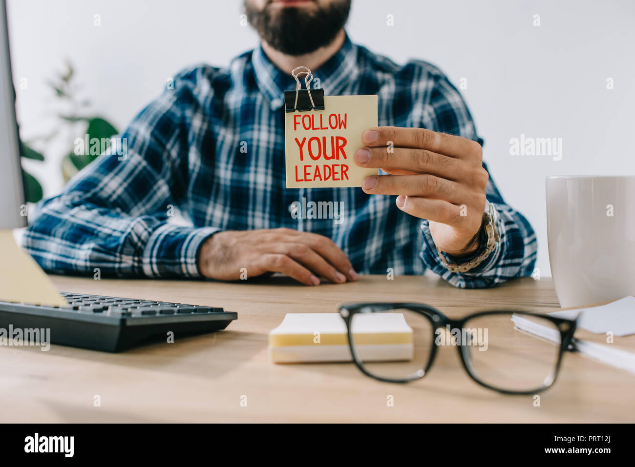 Ritagliato colpo di imprenditore di successo tenendo note adesive con 'Follow your leader' scritte Foto Stock