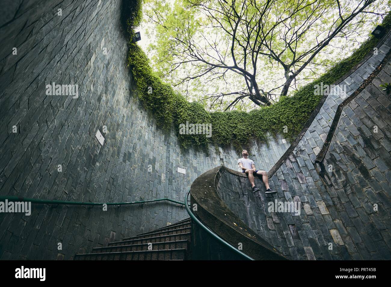Lonely Man seduto sulla scalinata a spirale dal passaggio pedonale sotterraneo in Singapore. Foto Stock