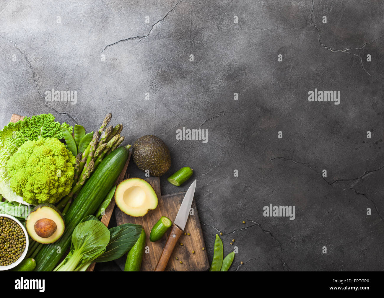 Assortiti nei toni del verde materie biologica di verdure in scatola in legno sulla pietra scura sullo sfondo. Avocado, Cavoli, cavolfiori e cetriolo con fagioli rifilate e Foto Stock