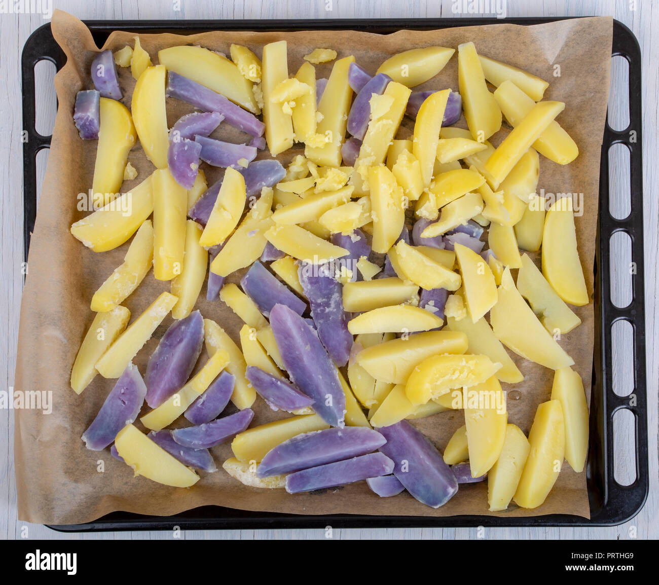 Materie sbucciate e tagliate a fette il blu e il giallo di patate su una teglia da forno Foto Stock