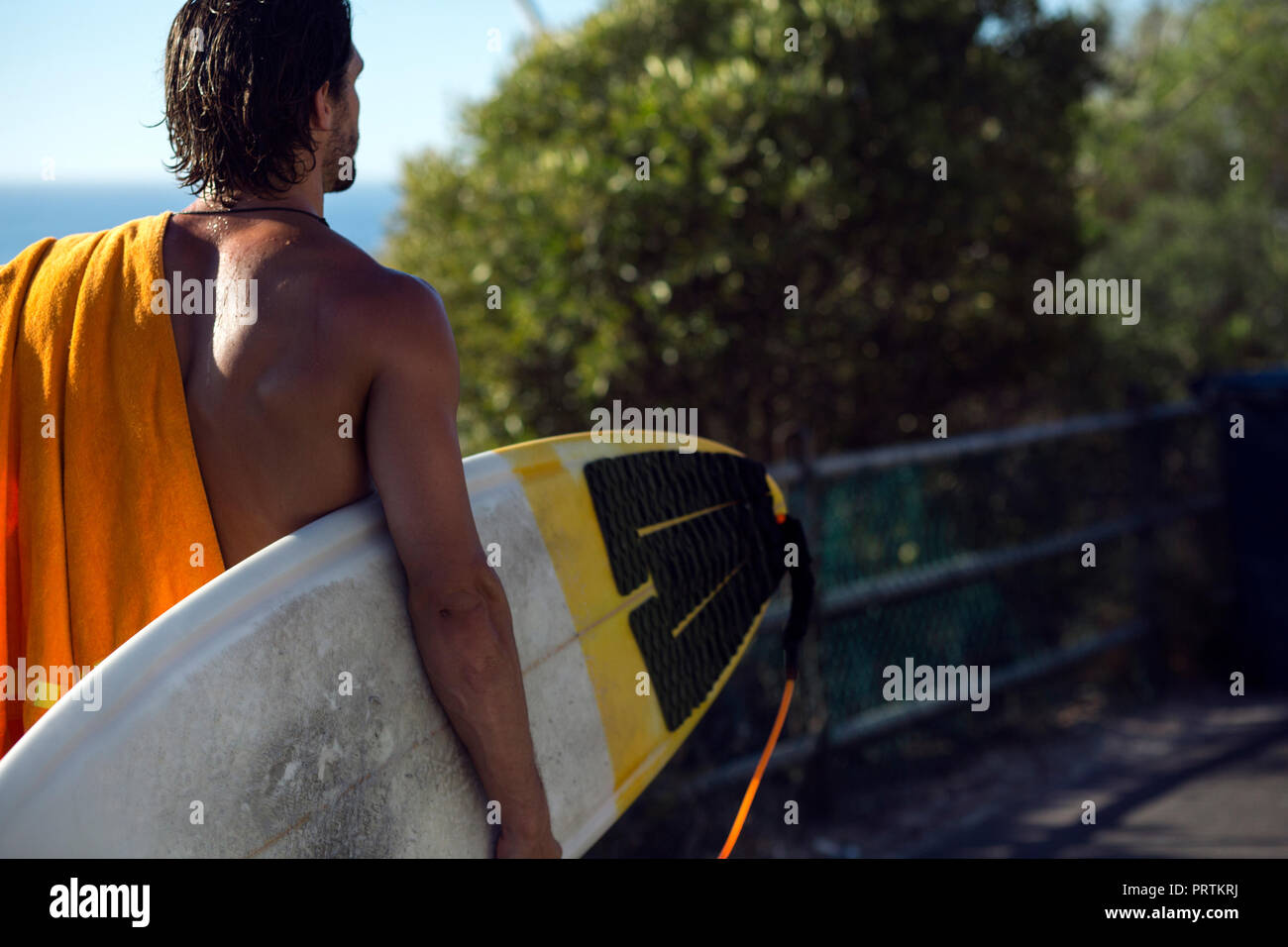 Metà maschio adulto surfer che trasportano le tavole da surf lungo la passeggiata sulla spiaggia, vista posteriore, spiaggia di Camps Bay, Città del Capo, Sud Africa Foto Stock