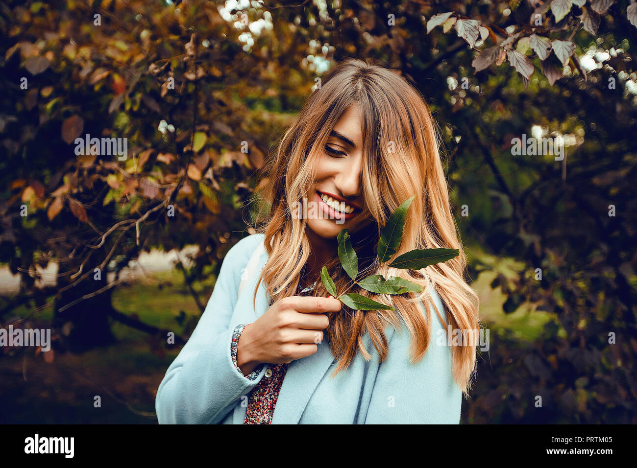 Donna con capelli lunghi biondi holding rametto di foglie in park, ritratto Foto Stock