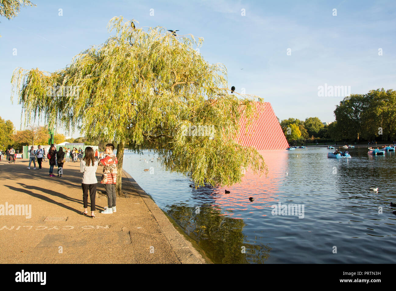 Una giovane coppia sostare davanti a un salice piangente albero accanto a Christo e Jeanne-Claude è il London Mastaba, su Londra la serpentina, London, Regno Unito Foto Stock