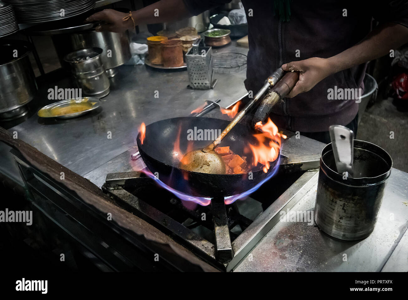 Lo chef cucinare con il fuoco con la padella. Chef per frittura in Padella fiammante sul piano di cottura a gas. street cafe con cibo di strada in India. Foto Stock