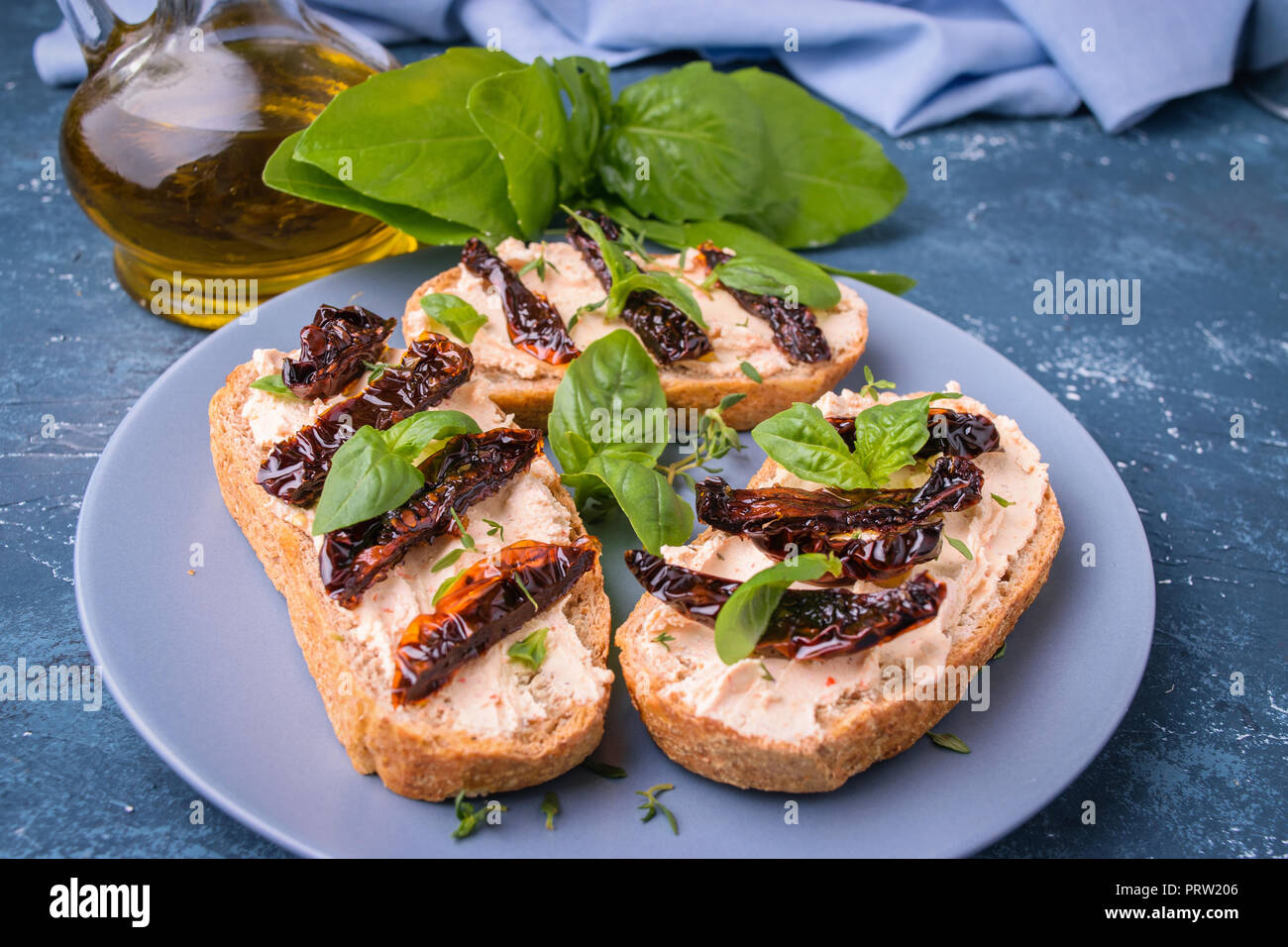 Tostare sandwich (bruschetta) con crema di formaggio, fette di pomodoro secco e le foglie di basilico. Sulla piastra di blu. Pasto delizioso. Foto Stock