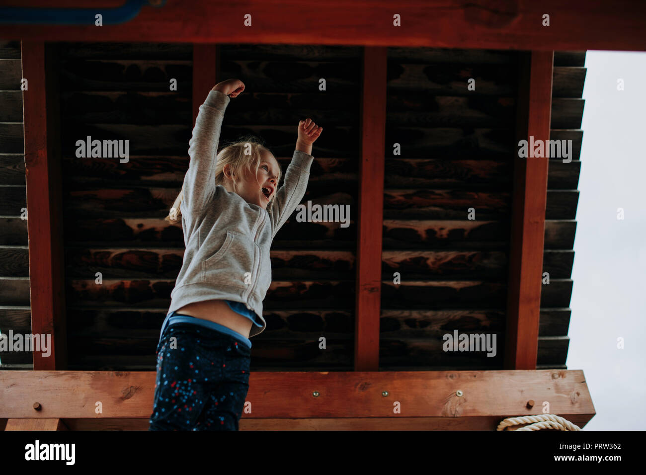 Ragazza saltando con le braccia sollevate sulla piattaforma di giochi per bambini Foto Stock