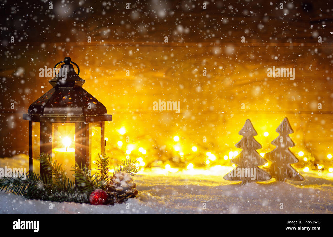 Scena di Natale con una lanterna, alberi, ramo di abete, fiocchi di neve e sfocate luci nella parte anteriore di un illuminato in legno scuro board come copia di spazio. Foto Stock