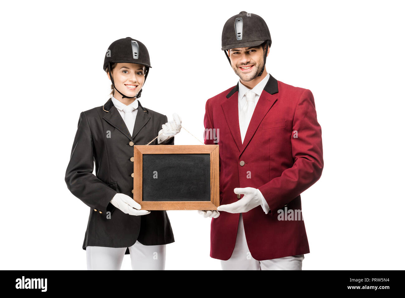 Sorridente equestrians giovani in uniforme e caschi holding blank board e guardando la telecamera isolato su bianco Foto Stock