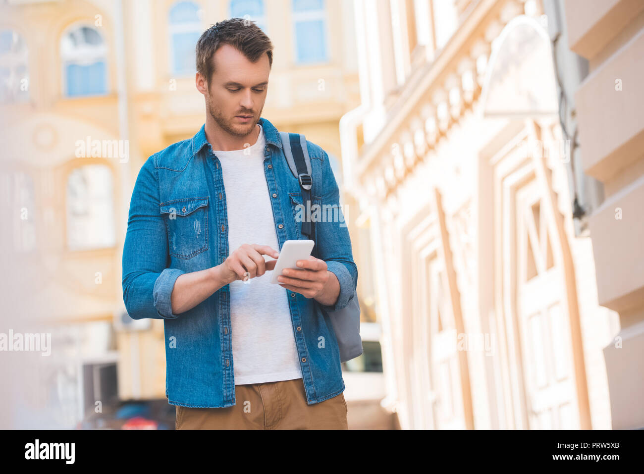Ritratto di focalizzato l uomo in denim shirt utilizza lo smartphone su strada Foto Stock