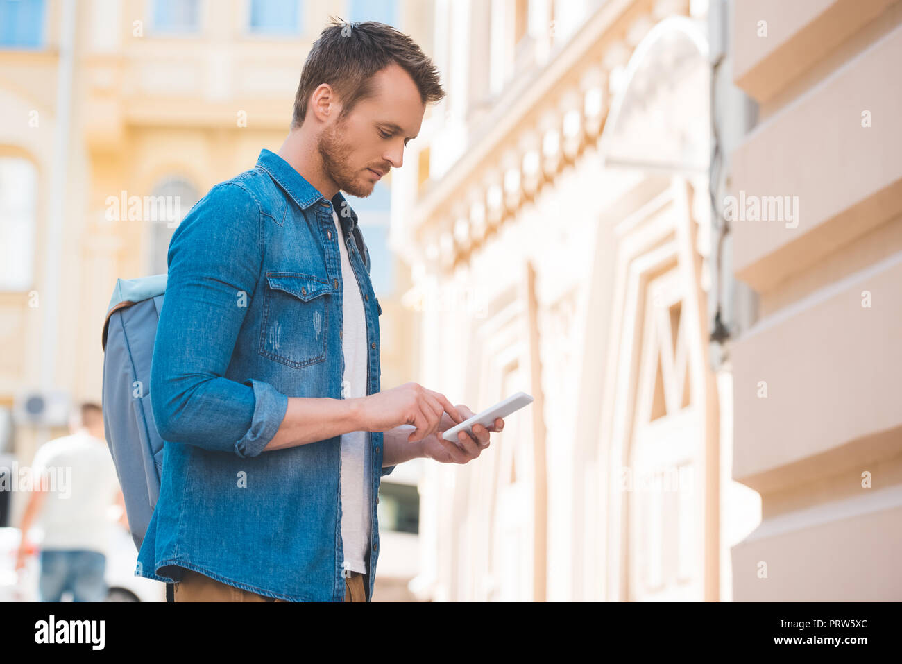 Vista laterale dell'uomo in denim shirt utilizza lo smartphone su strada Foto Stock