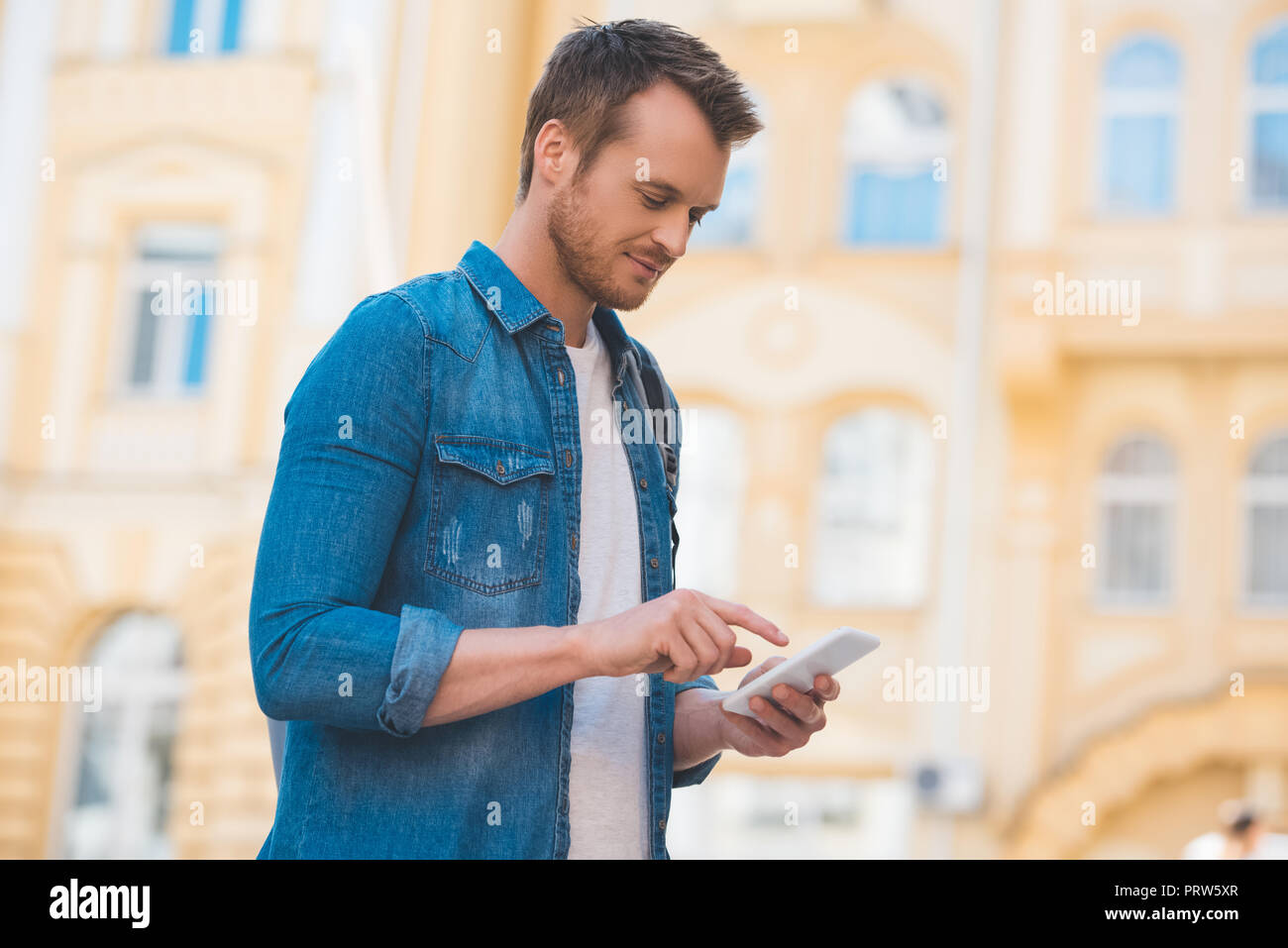 Vista laterale dell'uomo in denim shirt utilizza lo smartphone su strada Foto Stock