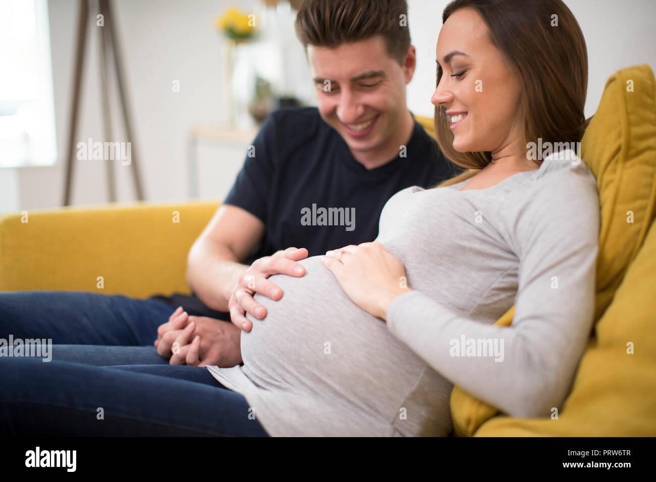 Incinta giovane seduto sul divano con uomo toccando Womans Stomaco Foto Stock