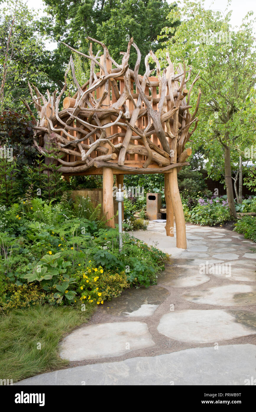 Grande pietra boulder lastra lastricato sentiero che conduce al nido in legno treehouse realizzato da driftwood, visualizzazione di superficie piantata in seguito con Epimediums, felci, Gerani Foto Stock