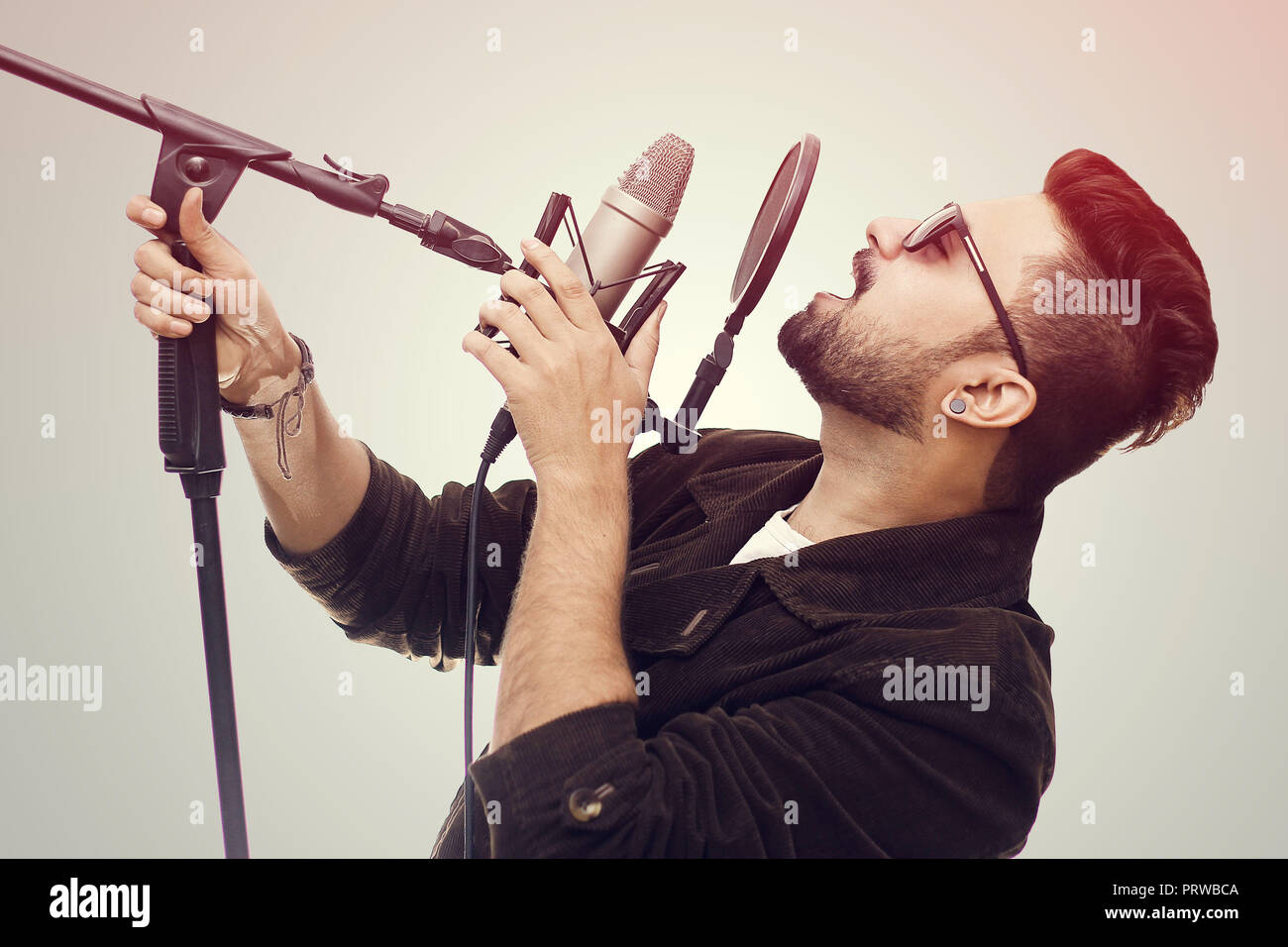 Talentuoso giovane uomo che indossa un cappotto marrone e bicchieri di cantare una canzone in studio di registrazione Foto Stock