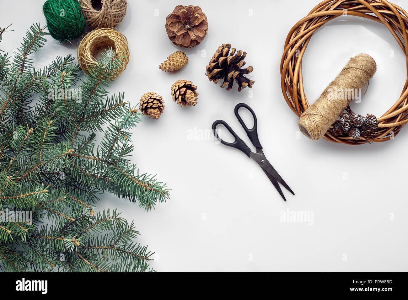 Bella festa ghirlanda fatta a mano base con tre colpi in prossimità di essa, fili e rametti di blu albero di Natale sul tavolo bianco sfondo, laici piana. Foto Stock