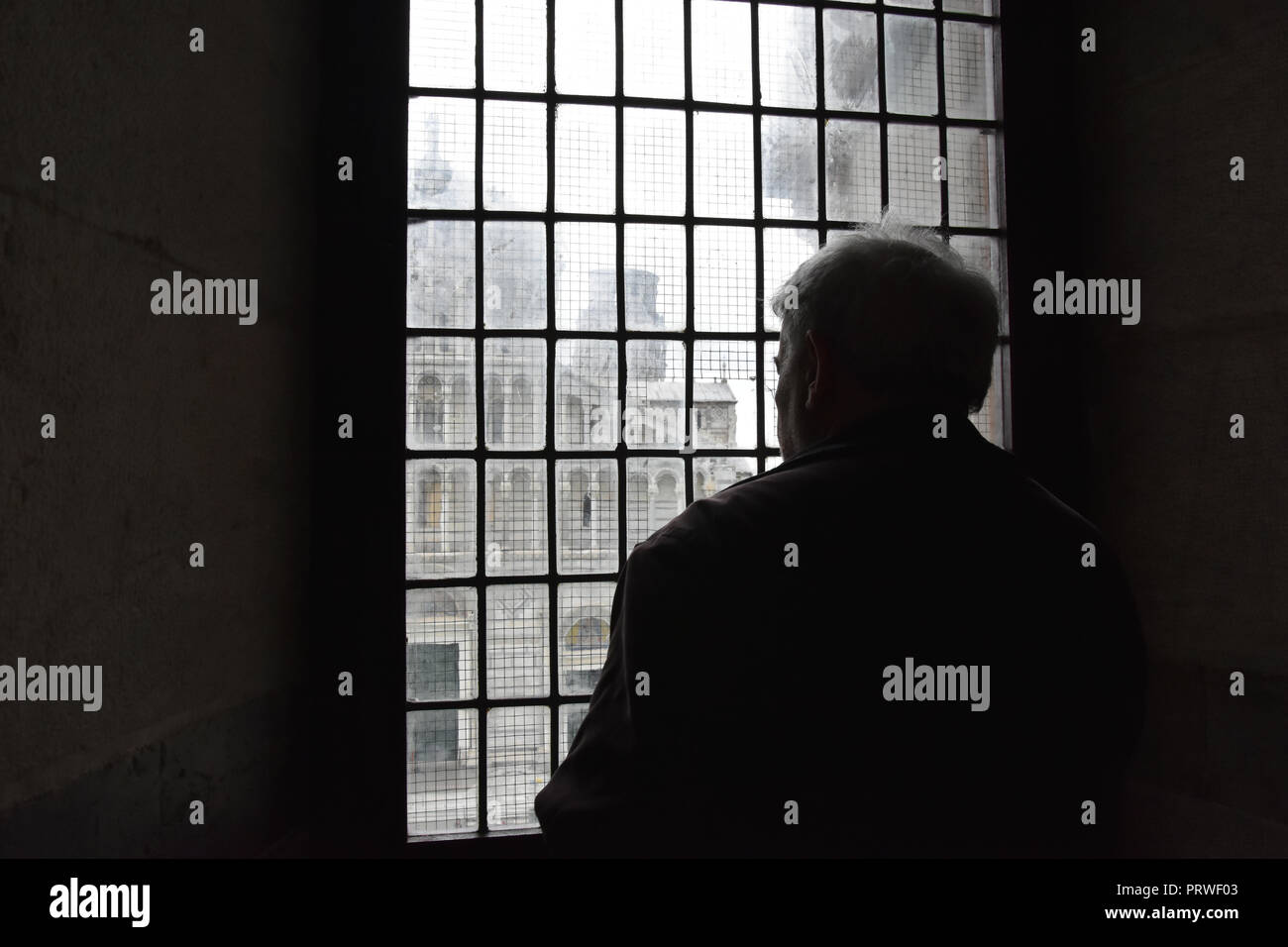Sagoma scura di un uomo anziano di guardare attraverso una finestra di Pisa il Battistero, Italia. La cattedrale di Pisa appena visto al di fuori Foto Stock