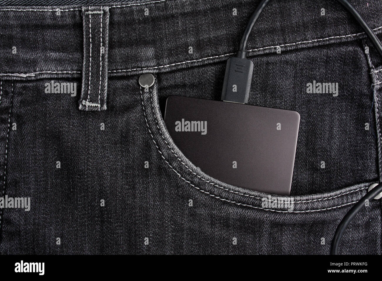 Nero un disco rigido portatile con cavo nel caso si trova nella tasca anteriore dei jeans neri Foto Stock